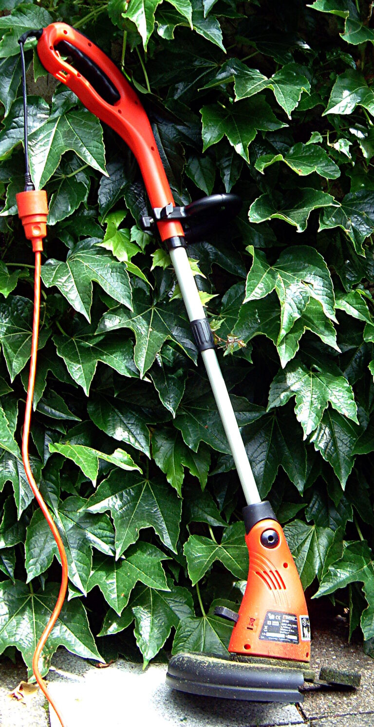 Electric string trimmer (grass trimmer) with power cord leaning against a hedge